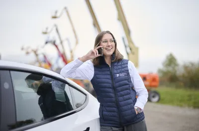 Sales representative from Platform Parts on the phone near a white car, with aerial work platforms in the background.